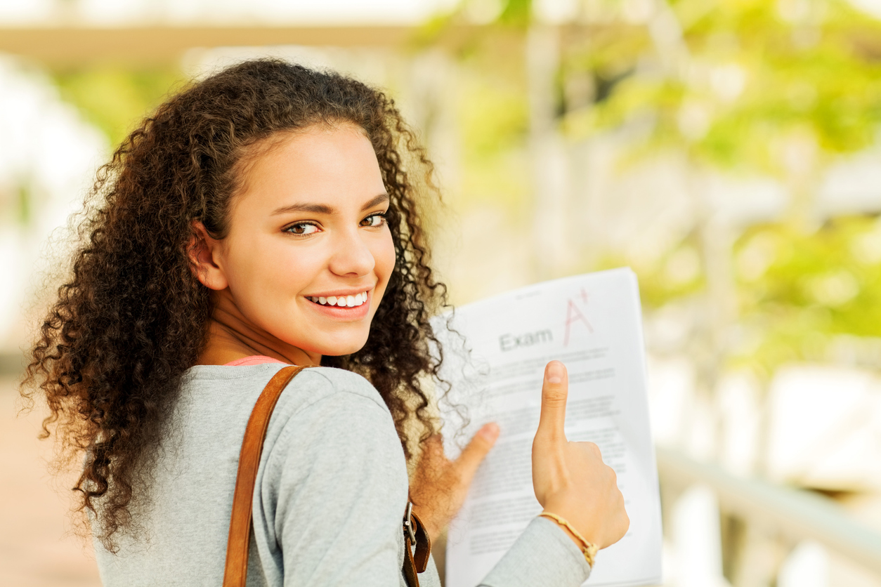 A smiling student proudly pointing at an exam paper marked with an A+ grade
