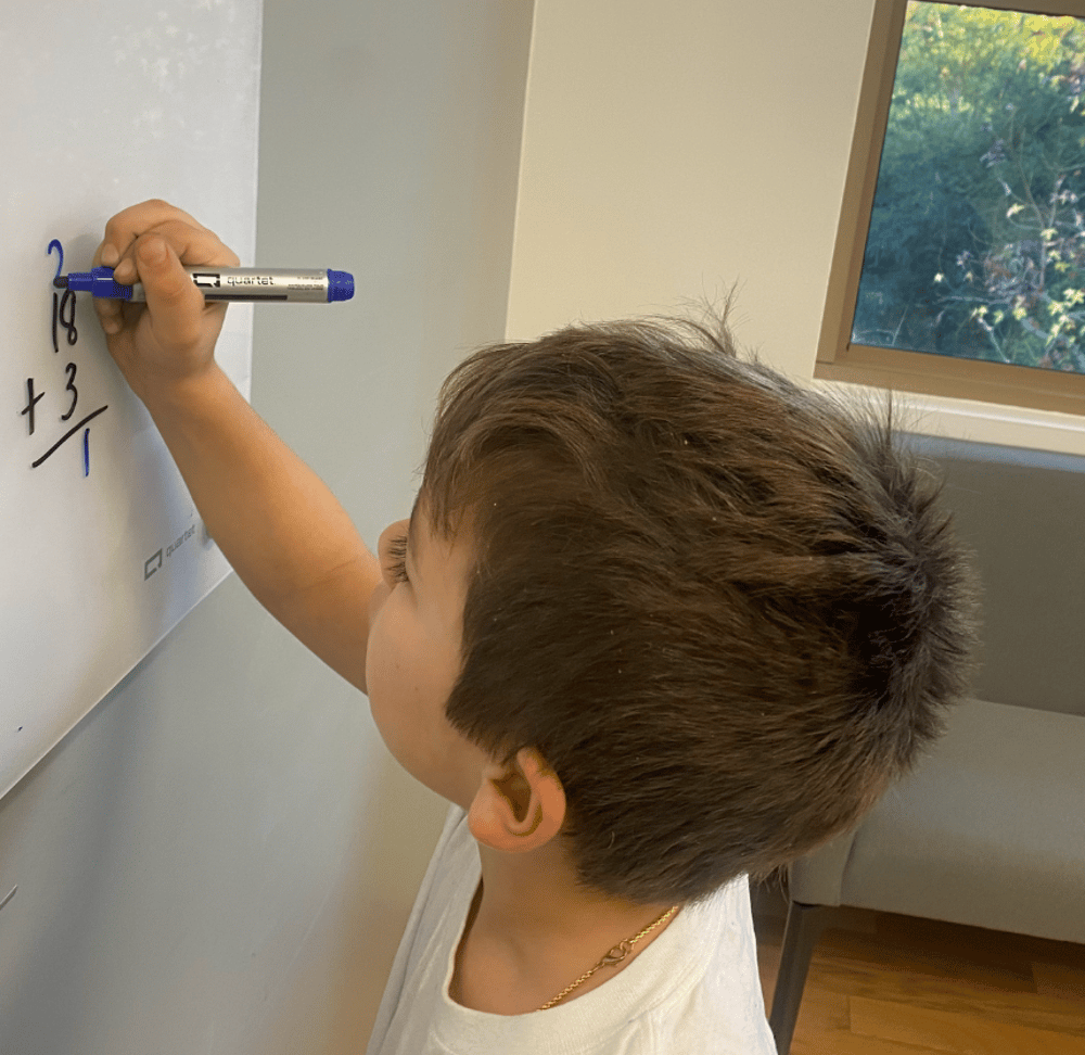 A young student solving an addition problem on a whiteboard