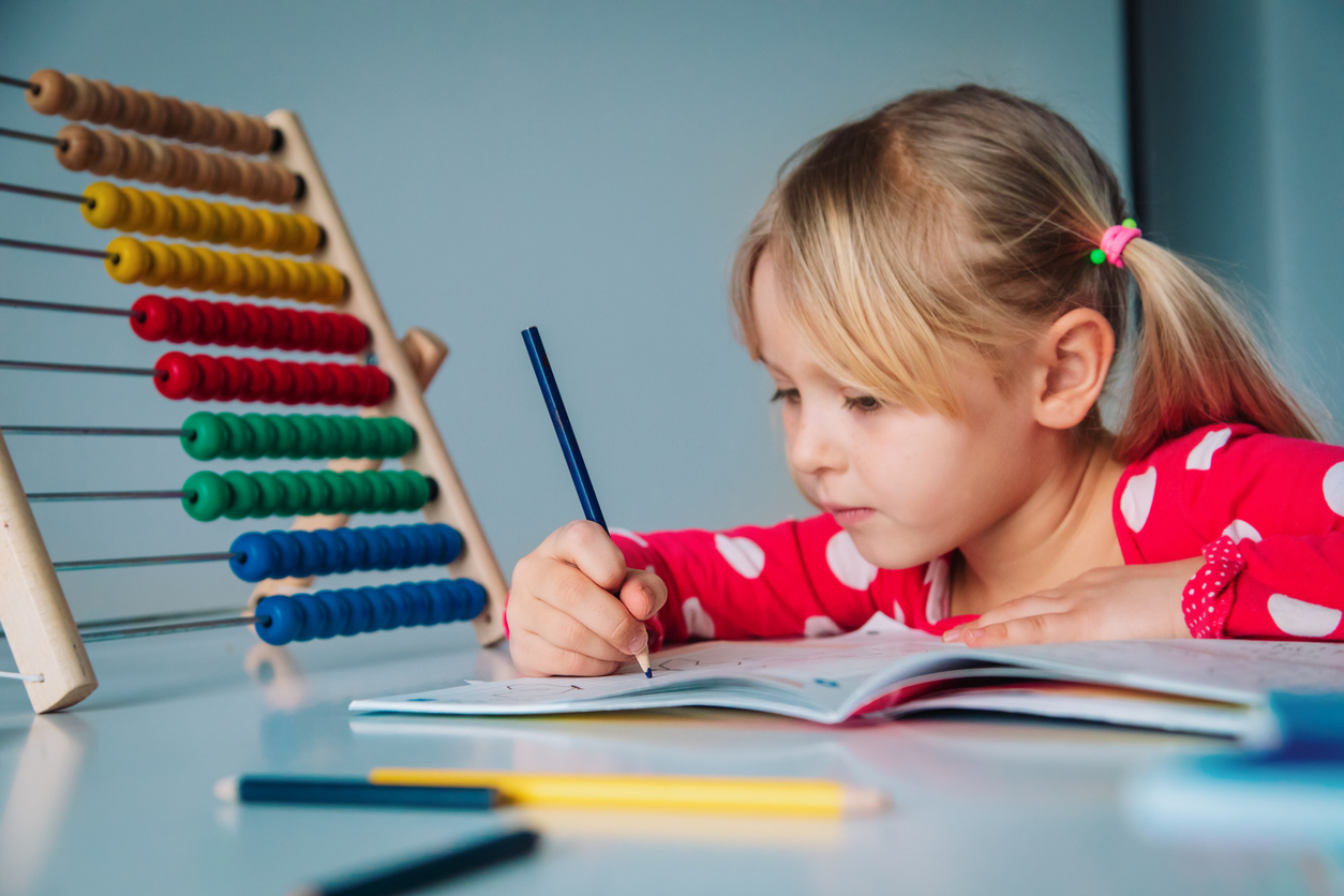 A young student practicing early math, writing in a workbook next to a colorful abacus